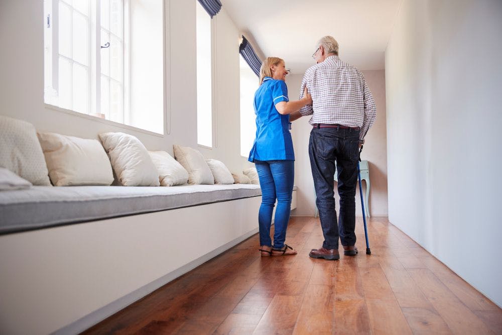 Nurse helping elderly man walk using a walking stick