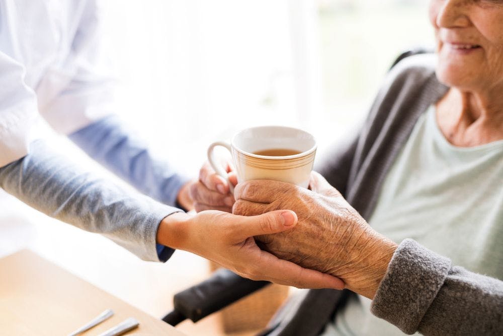Close up of a health care assistant giving a cup of tea to an elderly woman sat at a table